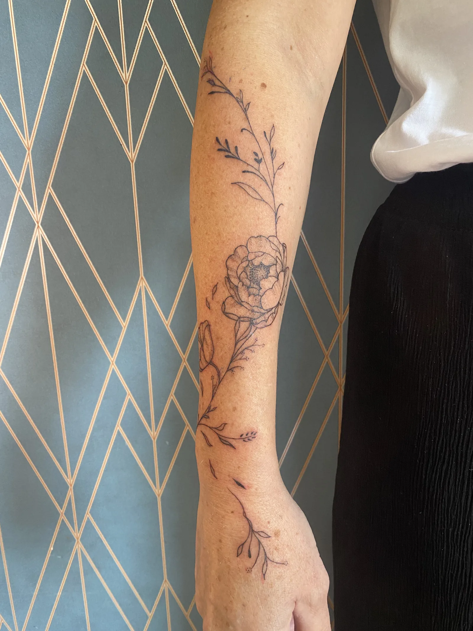 Tatouage pivoine et tiges florales fine line sur avant-bras — Annahata